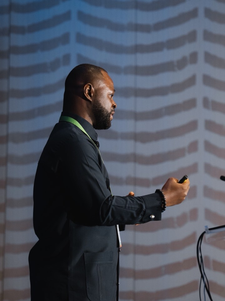 Speaker mid-presentation in front of a backdrop